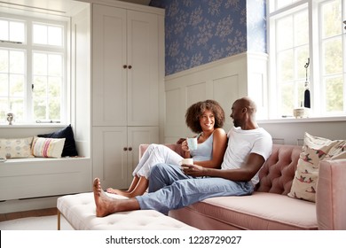 Young Black Couple Sitting Together On Couch In Living Room Drinking Coffee And Talking In The Morning, Low Angle, Full Length