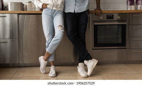 Young Black Couple In Stylish Casual Clothing Posing At Home Crossing Legs In Trendy Sport Shoes. Close Up Cropped View Of African Spouses Cleaning Company Customers Satisfied With Tidy Clean Kitchen