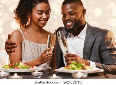 Young black couple toasting with champagne while having dinner at restaurant, close up