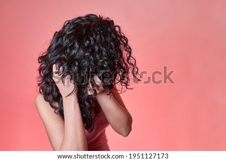 young black curly haired woman combing her hair following curly girl method on pink background. hair care concept.