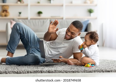 Young Black Dad And His Cute Infant Making Video Call With Laptop At Home, Adorable Little African American Toddler Sitting On Floor Next To Father, Man Waving Hand At Web Camera, Closeup