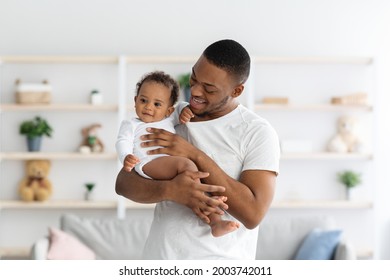 Young Black Dad Holding His Adorable Newborn Baby, Tenderly Embracing Infant Child While Relaxing Together At Home, African Father Bonding With Little Son Or Daughter, Enjoying Fatherhood, Free Space