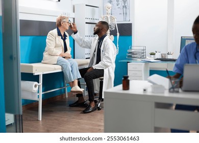 Young black doctor checking temperature of retired female patient during medical examination. African american male physician using thermometer on white old woman in medical office. - Powered by Shutterstock