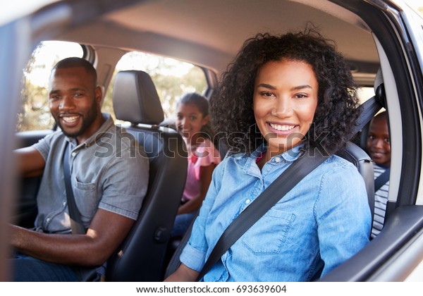 Young black family in a car on a road trip smiling\
to camera