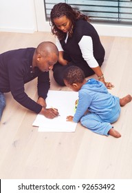 Young Black Family Sitting On The Floor Drawing A Picture With Their Son.