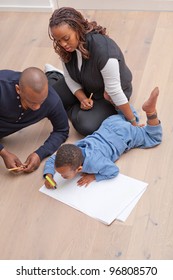 Young Black Family Sitting On The Floor Drawing A Picture With Their Son.