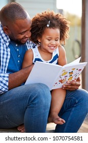 Young black father and daughter reading book outside - Shutterstock ID 1070754581