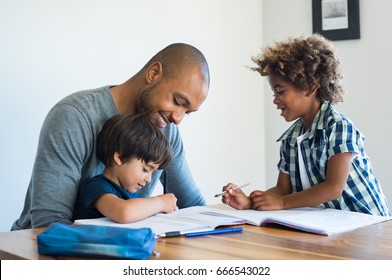 Young Black Father Helping His Boys With Homework. Multiethnic Brothers Studying With Their Dad At Home. Two Cute Children Doing Homeworks With The Help Of Their Loving Parent.