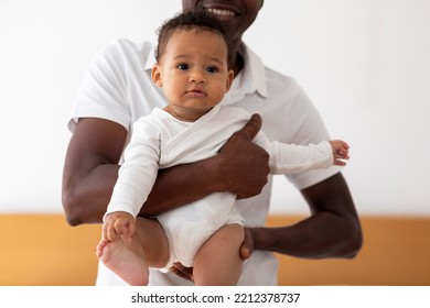 Young Black Father Holding Cute Little Baby Boy In Hands, Loving African American Dad Embracing His Small Infant Son And Smiling, Bonding With Adorable Newborn Child At Home, Closeup Shot