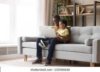 Young black father and kid son using laptop at home for child education looking at pc screen doing online shopping at home, smiling african dad and toddler boy study learning computer watching video