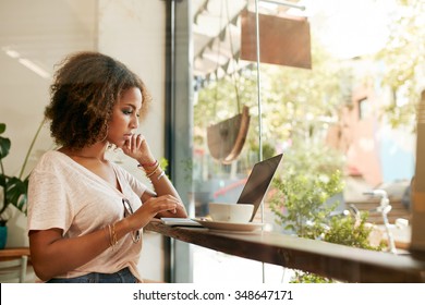 Young Black Female At Cafe Using Laptop. African Young Woman Sitting In A Restaurant Busy Working On Her Laptop.