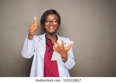 Young Black Female Doctor Carrying A Tablet Computer Smiling And Giving A Thumbs Up Gesture