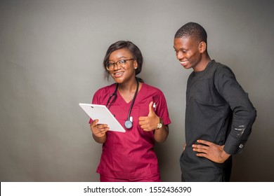 Young Black Female Doctor Holding A Tablet Computer Standing With A Young Black Man Gives A Thumbs Up, Both Of Them Are Smiling