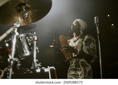 Young Black female jazz musician singing song and playing guiro during rehearsal in studio, low angle view - Powered by Shutterstock