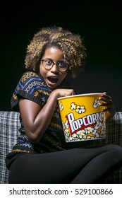 Young Black Girl Sitting On The Sofa Watching TV With Popcorn