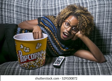 Young Black Girl Sitting On The Sofa Watching TV With Popcorn