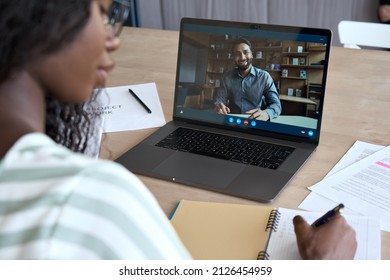 Young black girl student having virtual remote class with distance indian teacher teaching training webinar or tutor on video call using laptop computer learning online at home. Over shoulder view - Powered by Shutterstock