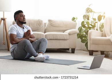 Young Black Guy Meditating In Front Of Laptop At Home, Watching Yoga Tutorials Online, Sitting In Lotus Position In Living Room, Copy Space - Powered by Shutterstock