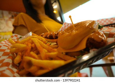 Young Black Haired Girl Holding A Tray Of Junk Food. Brunette Holding Fries And Cheeseburger. Delicious Potatoes And Burgers On A Tray. Spicy Chicken Tender. Waitress Serving Fast Food. 