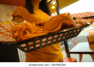 Young Black Haired Girl Holding A Tray Of Junk Food. Brunette Holding Fries And Cheeseburger. Delicious Potatoes And Burgers On A Tray. Spicy Chicken Tender. Waitress Serving Fast Food. 