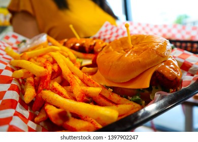 Young Black Haired Girl Holding A Tray Of Junk Food. Brunette Holding Fries And Cheeseburger. Delicious Potatoes And Burgers On A Tray. Spicy Chicken Tender. Waitress Serving Fast Food. 