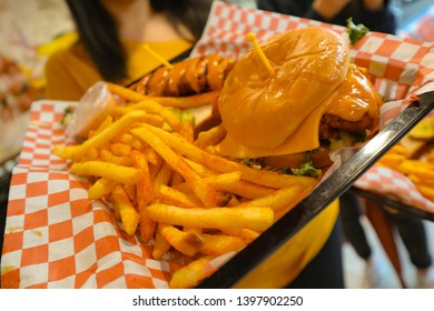 Young Black Haired Girl Holding A Tray Of Junk Food. Brunette Holding Fries And Cheeseburger. Delicious Potatoes And Burgers On A Tray. Spicy Chicken Tender. Waitress Serving Fast Food. 