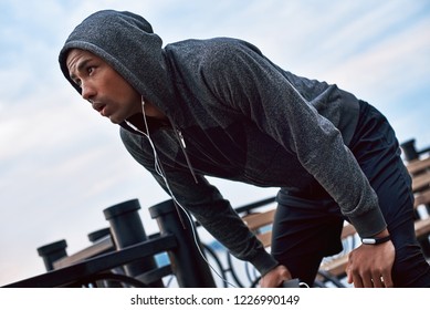 Young black jogger in the hood is stopped to have a little rest before long distance running. He wears a sports jacket with hood - Powered by Shutterstock