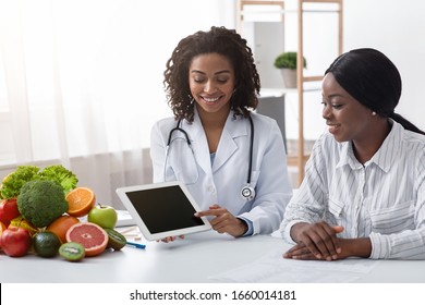 Young Black Lady Doctor Consultating Patient, Using Digital Tablet In Office, Making Patient's Anamnesis, Copy Space