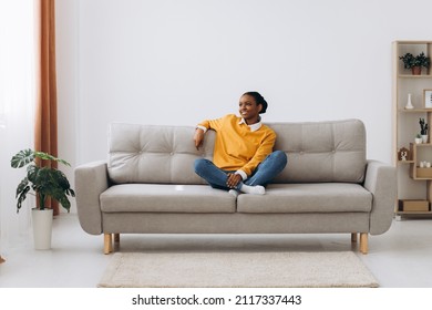 Young Black Lady Enjoying Weekend And Relaxing On Comfortable Couch At Home. African American Woman Sitting On Sofa In Living-room, Stretching Arms And Smiling Feeling Untroubled And Happy, Back View