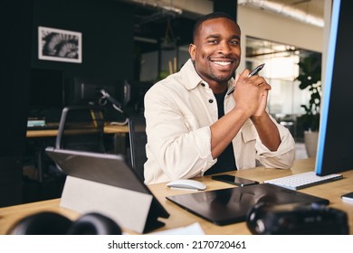 Young Black Male Advertising Marketing Or Design Creative In Modern Office Sitting At Desk Working On Computer Smiling to Camera