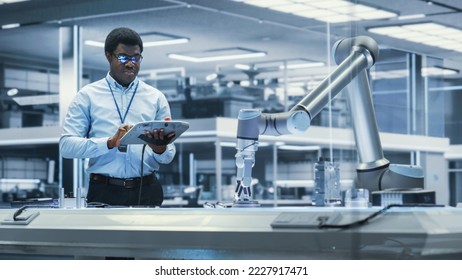 Young Black Male Engineer Using a Tablet Computer, Researching and Developing a Futuristic Robotic Arm Machine in a High Tech Industrial Laboratory with Modern Equipment. - Powered by Shutterstock