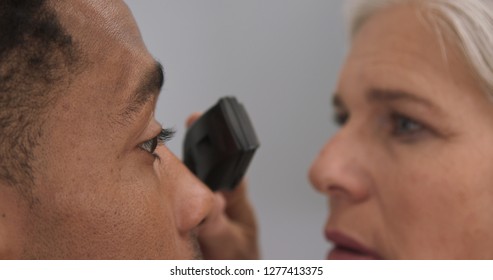 Young Black Male Patient Having His Eyes Checked By Senior Female Doctor