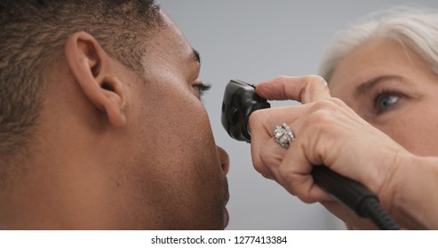 Young Black Male Patient Having His Eyes Checked By Senior Female Doctor