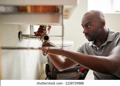 Young Black Male Plumber Sitting On The Floor Fixing A Bathroom Sink, Close Up