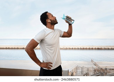 Young Black male runner taking a break to hydrate. African American man drinking water after exercising and jogging outdoors. Healthy lifestyle and sport concept. - Powered by Shutterstock