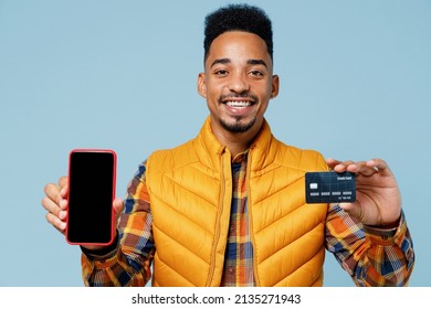 Young black man 20s wears yellow waistcoat shirt using mobile cell phone with blank screen workspace area hold in hand credit bank card isolated on plain pastel light blue background studio portrait - Shutterstock ID 2135271943
