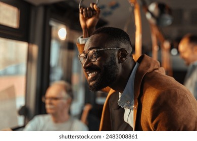 Young black man with a beard wearing eyeglasses holds onto a handrail while standing on a crowded public bus. - Powered by Shutterstock