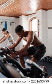 Young Black Man And Biracial Woman Cycling On Exercise Bike At The Gym