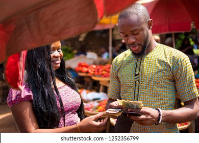 Young Black Man Counting Money To Give To A Woman In A Local African Market 