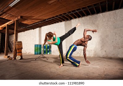 Young Black man dodging a Capoeria kick with berimbau player in back