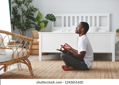 young black man doing yoga and sitting in lotus position at home in the bedroom