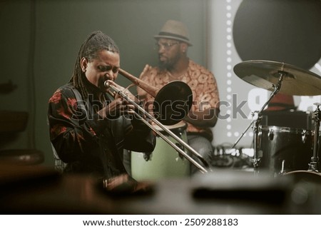 Young Black man with dreadlocks playing trombone during rehearsal or live performance in bar
