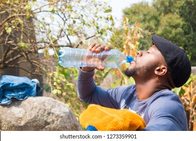 Young Black Man Drinking Water From A Plastic Bottle Outside 