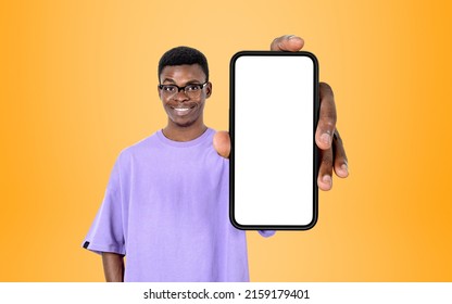 Young black man in eyeglasses smiling, showing phone with mock up copy space screen, yellow background. Concept of mobile app and social media - Shutterstock ID 2159179401