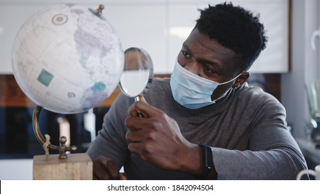 Young Black Man With Face Mask Looking At The Through Magnifying Glass. Travel Ban During Global Pandemic. High Quality Photo