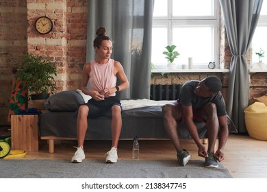 Young Black man and his Caucasian girlfriend sitting on sofa getting ready for exercising and jogging in morning - Powered by Shutterstock