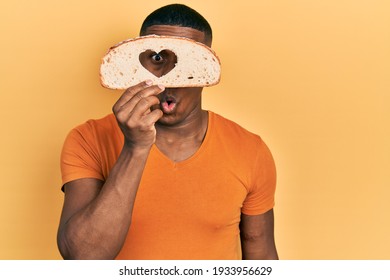 Young Black Man Holding Bread Loaf With Heart Shape Scared And Amazed With Open Mouth For Surprise, Disbelief Face 