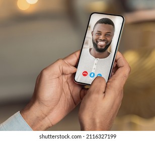 Young Black Man Holding Cell Phone In Hand Video Calling Distance Friend Online Looking On Mobile Screen Using Smartphone Videochat Application, Over Shoulder Closeup View, Selective Focus