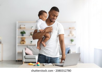 Young Black Man Holding Little Baby On Hands And Using Laptop At Home, Millennial African American Father Working Remotely With Computer While Babysitting His Adorable Infant Child, Copy Space