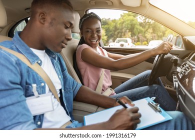 Young Black Man Instructor Examinating Happy Lady Student, Taking Notes At Chart While Sitting By Cheerful African American Woman Driving Auto, Side View, Copy Space, Sun Flare